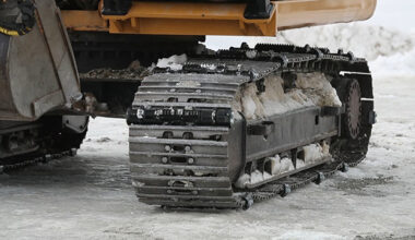 Excavator track rolling across ice with icegrip snow traction device attached
