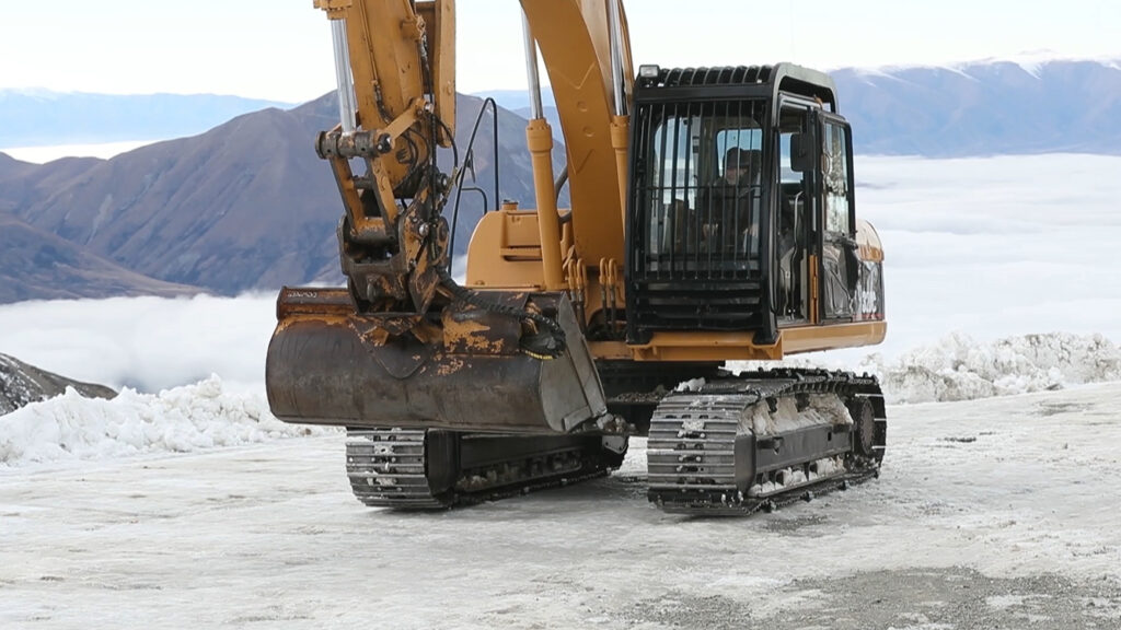 Excavator track rolling across ice with icegrip snow traction device attached