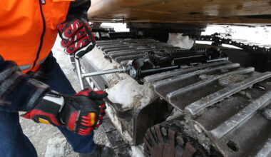 Person attaching an icegrip snow traction device to an excavator track on snowy site