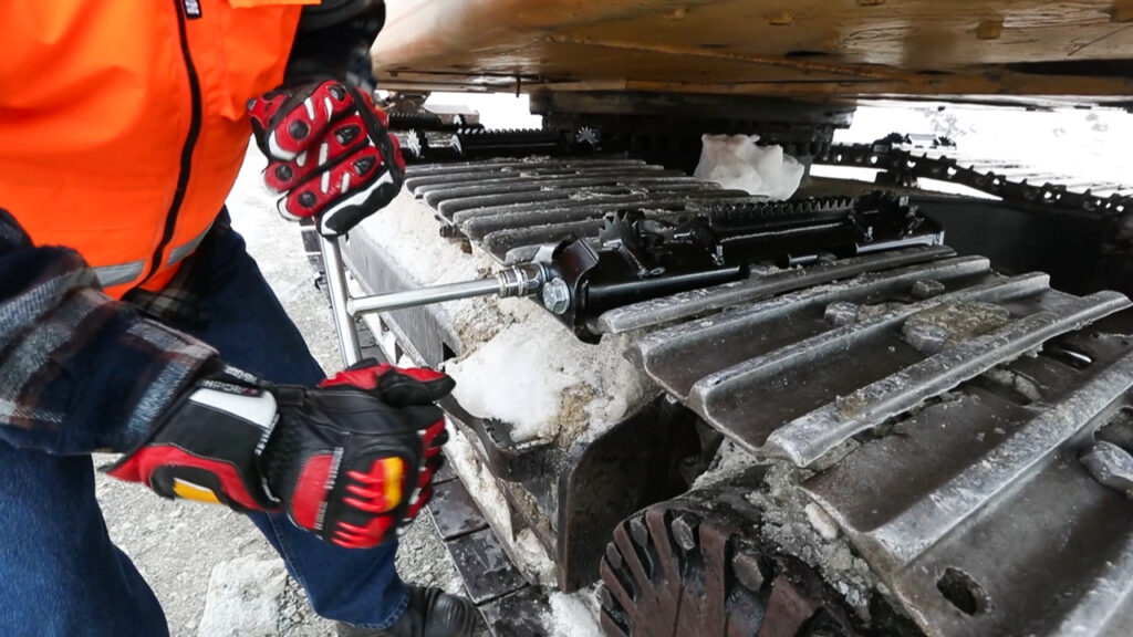 Person attaching an icegrip snow traction device to an excavator track on snowy site