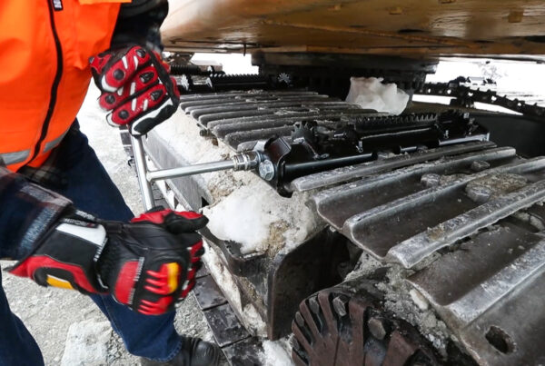 Person attaching an icegrip snow traction device to an excavator track on snowy site