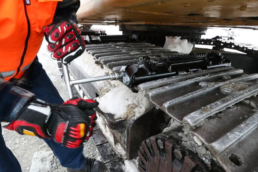 Person attaching an icegrip snow traction device to an excavator track on snowy site