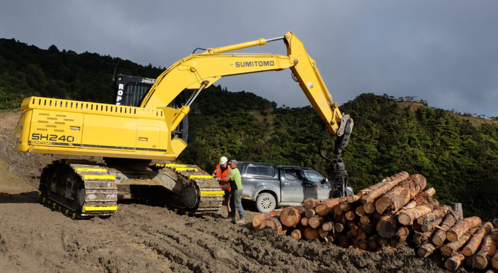 two people attaching excavator attachments on a sumitomo excavator track at a work site
