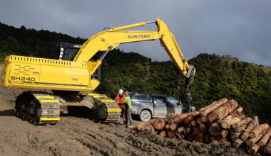 two people attaching excavator attachments on a sumitomo excavator track at a work site