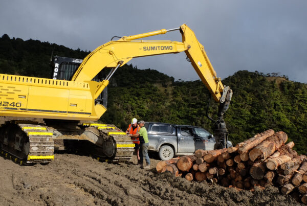 two people attaching excavator attachments on a sumitomo excavator track at a work site