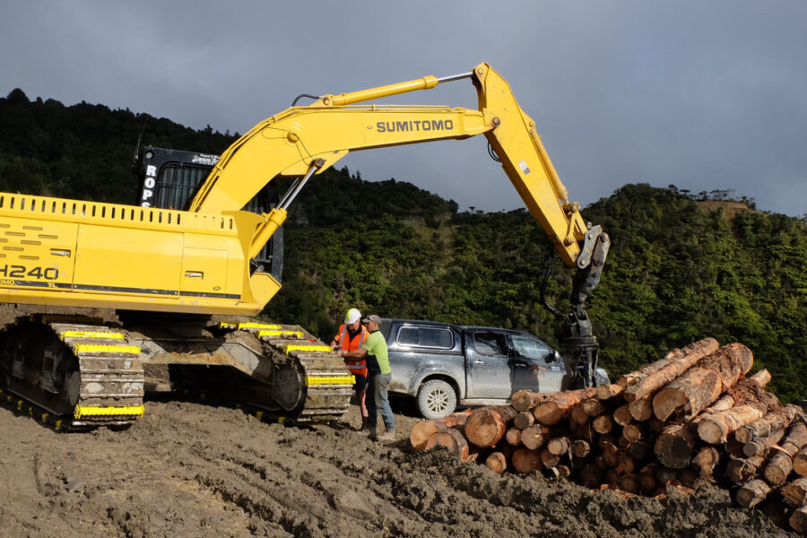 two people attaching excavator attachments on a sumitomo excavator track at a work site