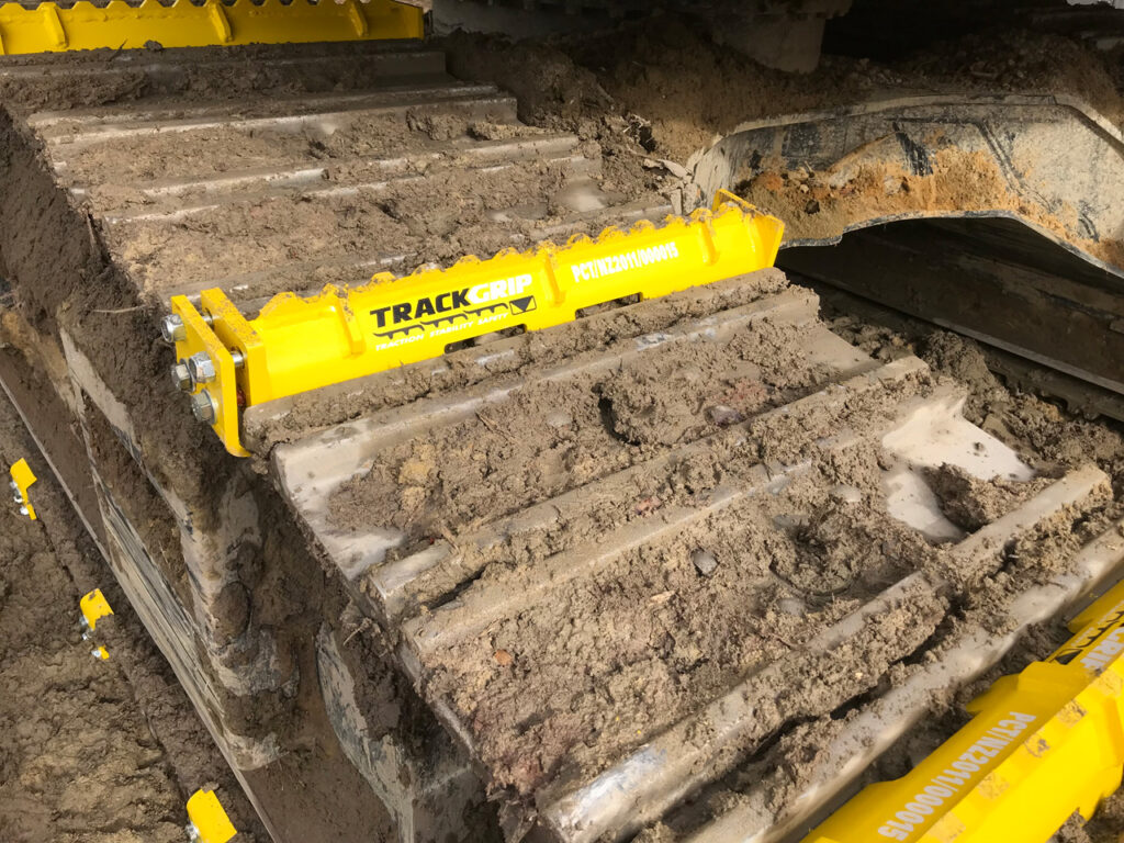 steel excavator track rolling along a dirt terrain with yellow mightygrip excavator track attachments